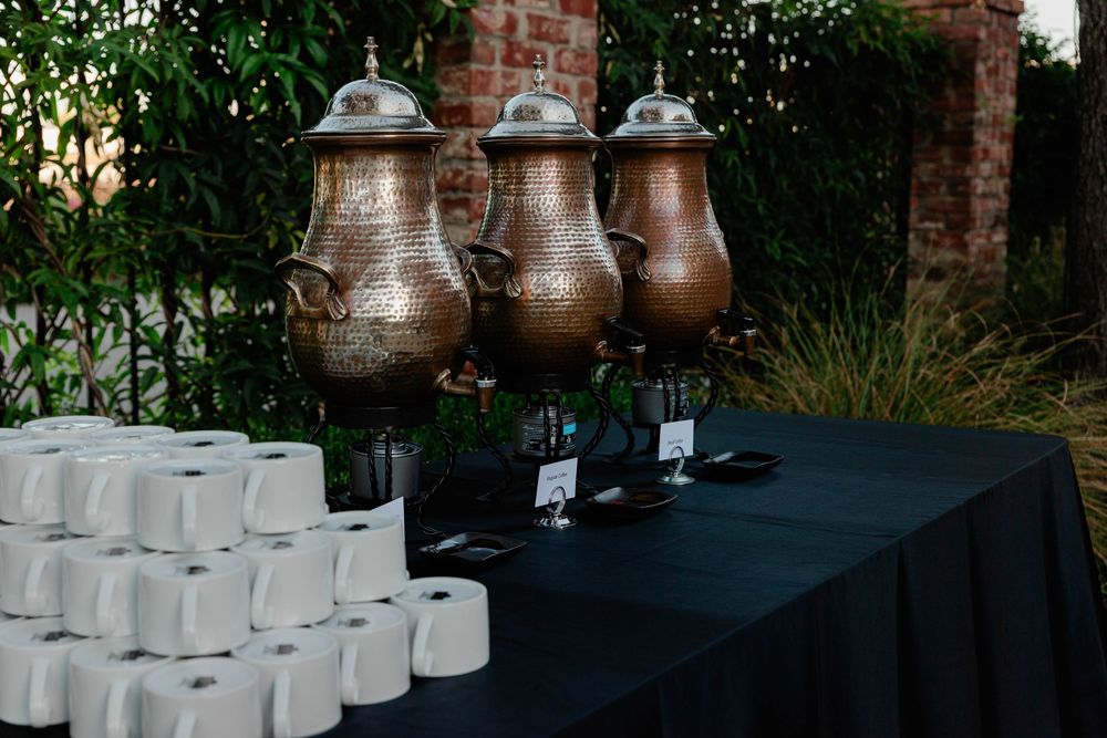 Row of glass drink dispensers set up on black tablecloth outdoors.