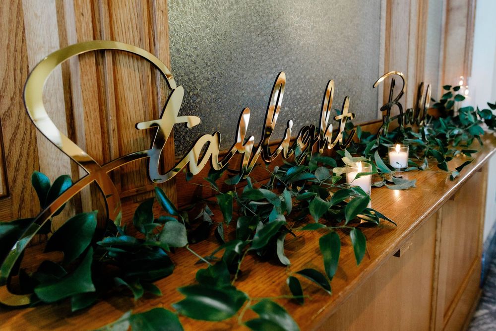 Decorative gold signage and greenery displayed along wooden wall.