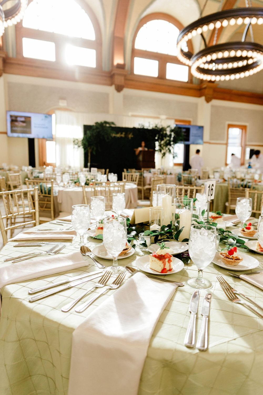 Formal banquet hall with white tablecloths and place settings under chandeliers.
