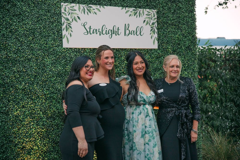 Outdoor social gathering with greenery wall backdrop and 'Starlight Ball' signage.