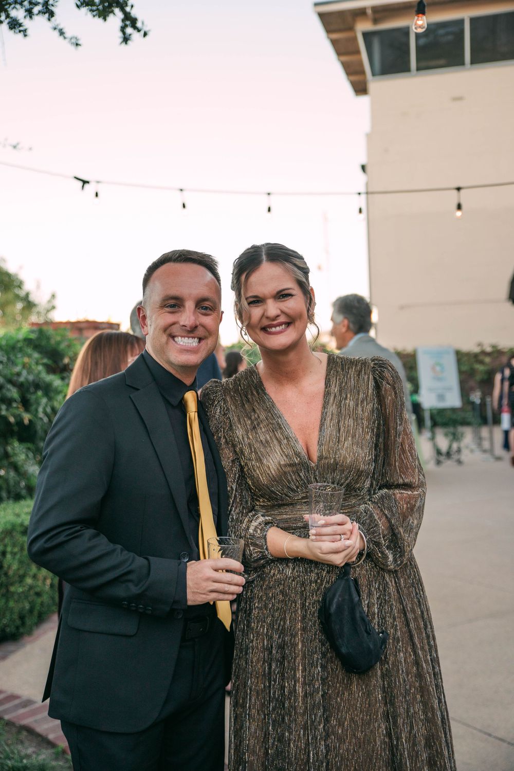 Evening social event with guests mingling outdoors against a backdrop of string lights.