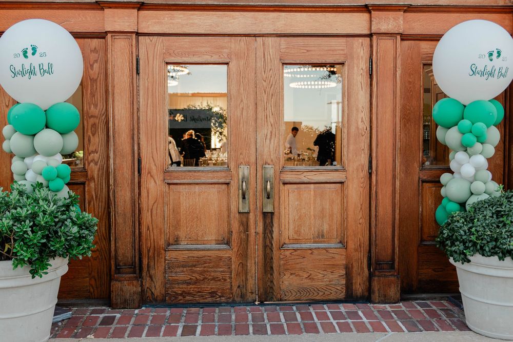Wooden entrance doors decorated with green and white balloon arrangements.