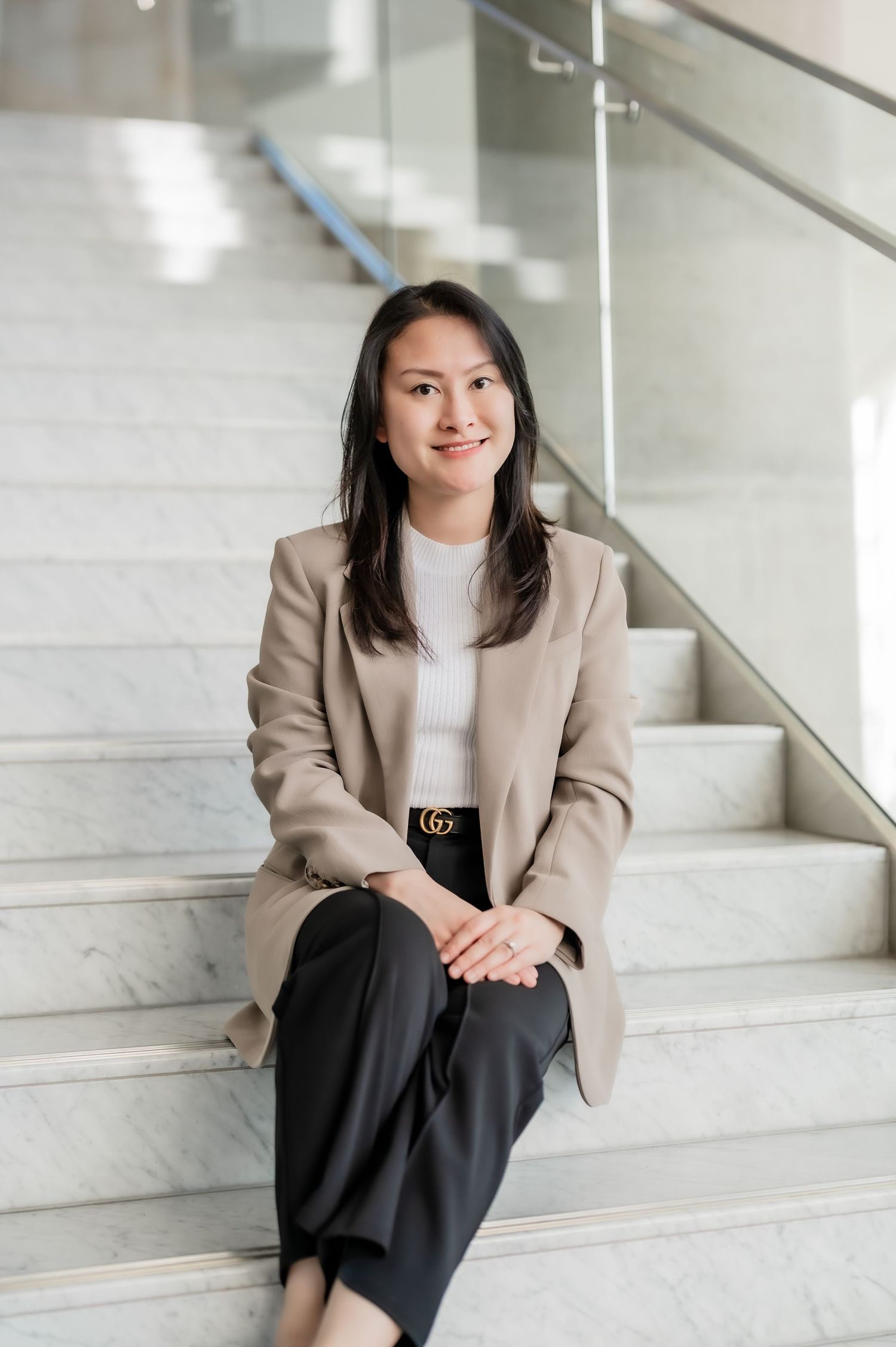 Professional seated on concrete stairs wearing a beige blazer, white top, and black skirt in modern office setting.