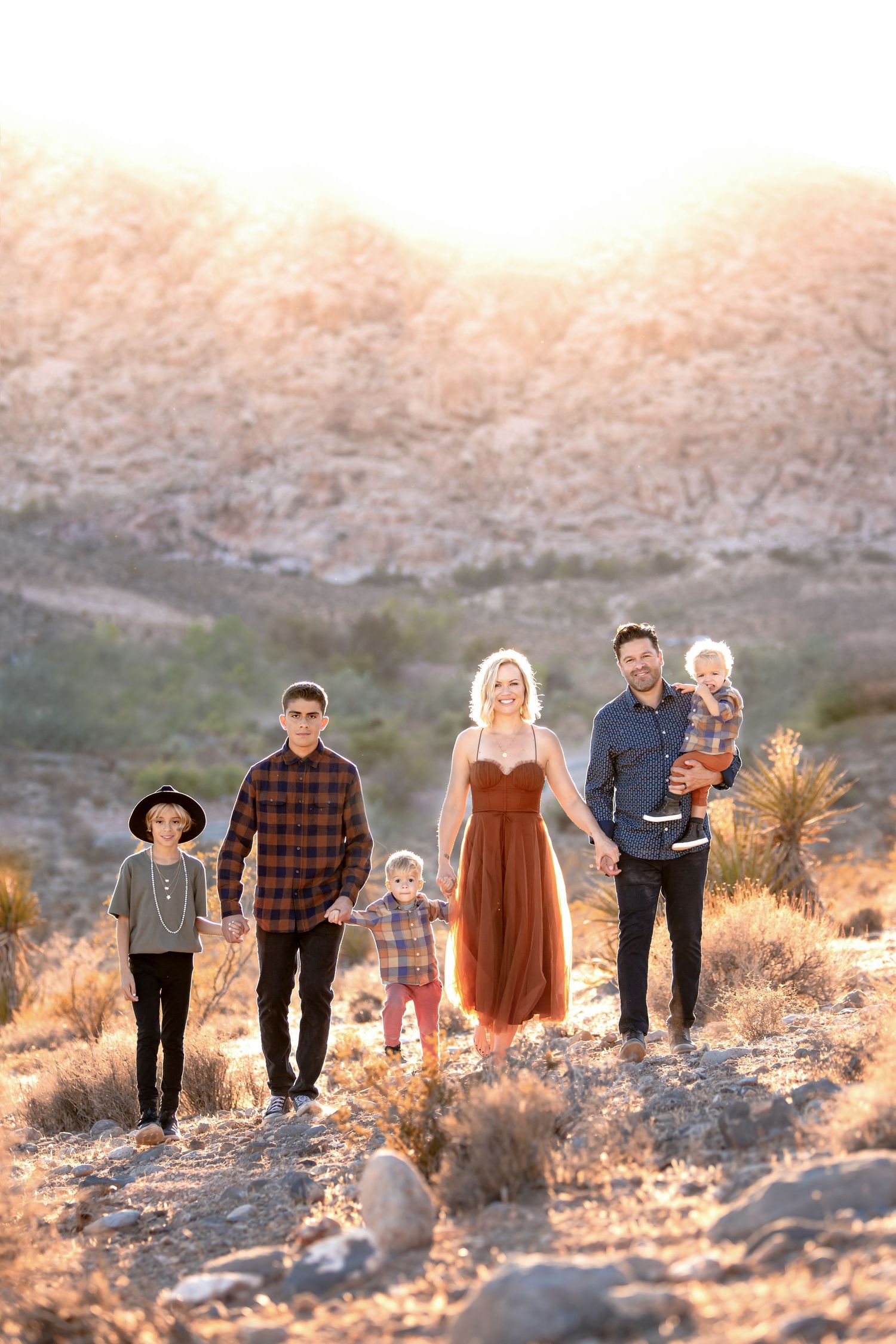 A group of people walk together along a desert path at sunset with mountains in the background.