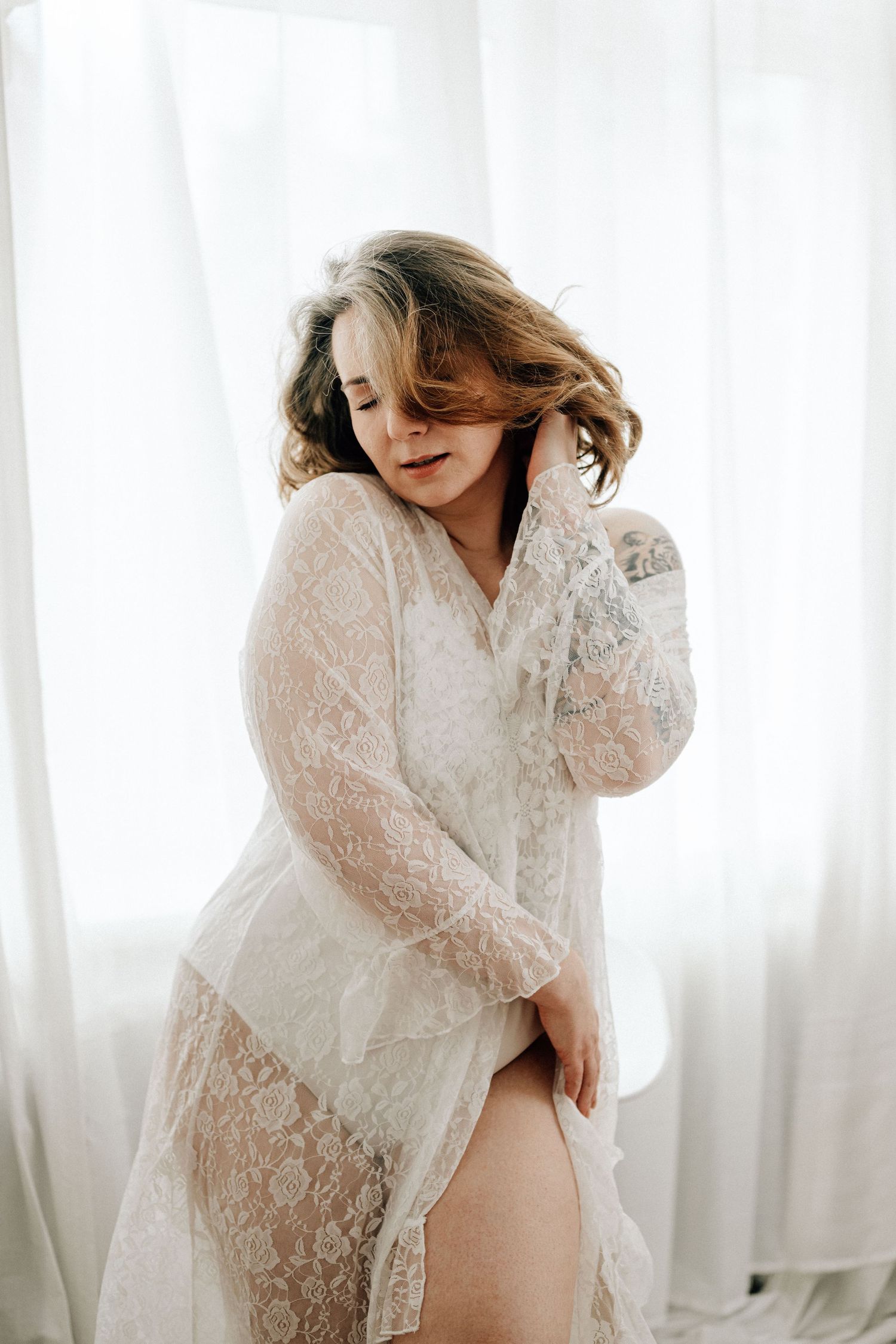 Boudoir Portrait in einer sinnlichen Pose einer Frau mit sanften Fensterlicht vor weißen Vorhängen