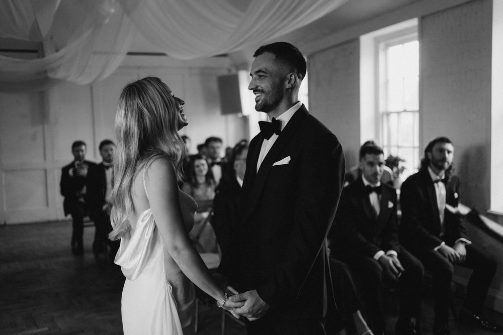A wedding party gathers in an elegant white room with arched windows and ornate architectural details at bourne and hollingsworth in London
