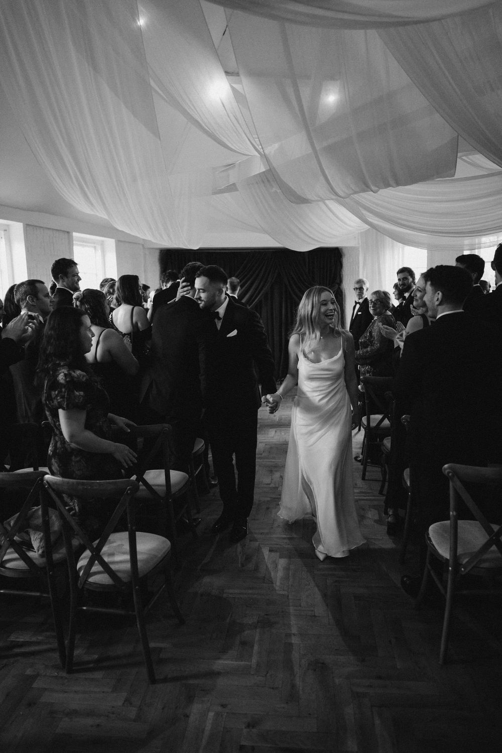 Wedding ceremony guests seated in an elegant draped white tent with overhead lighting.