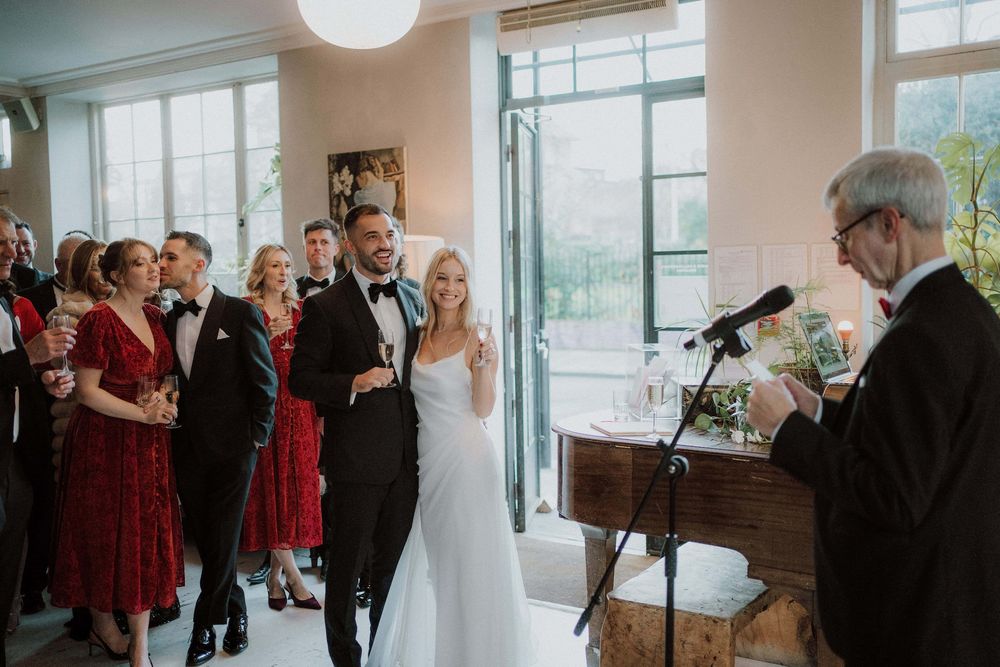 Wedding party celebrates in an elegant indoor venue with red bridesmaid dresses and formal attire.
