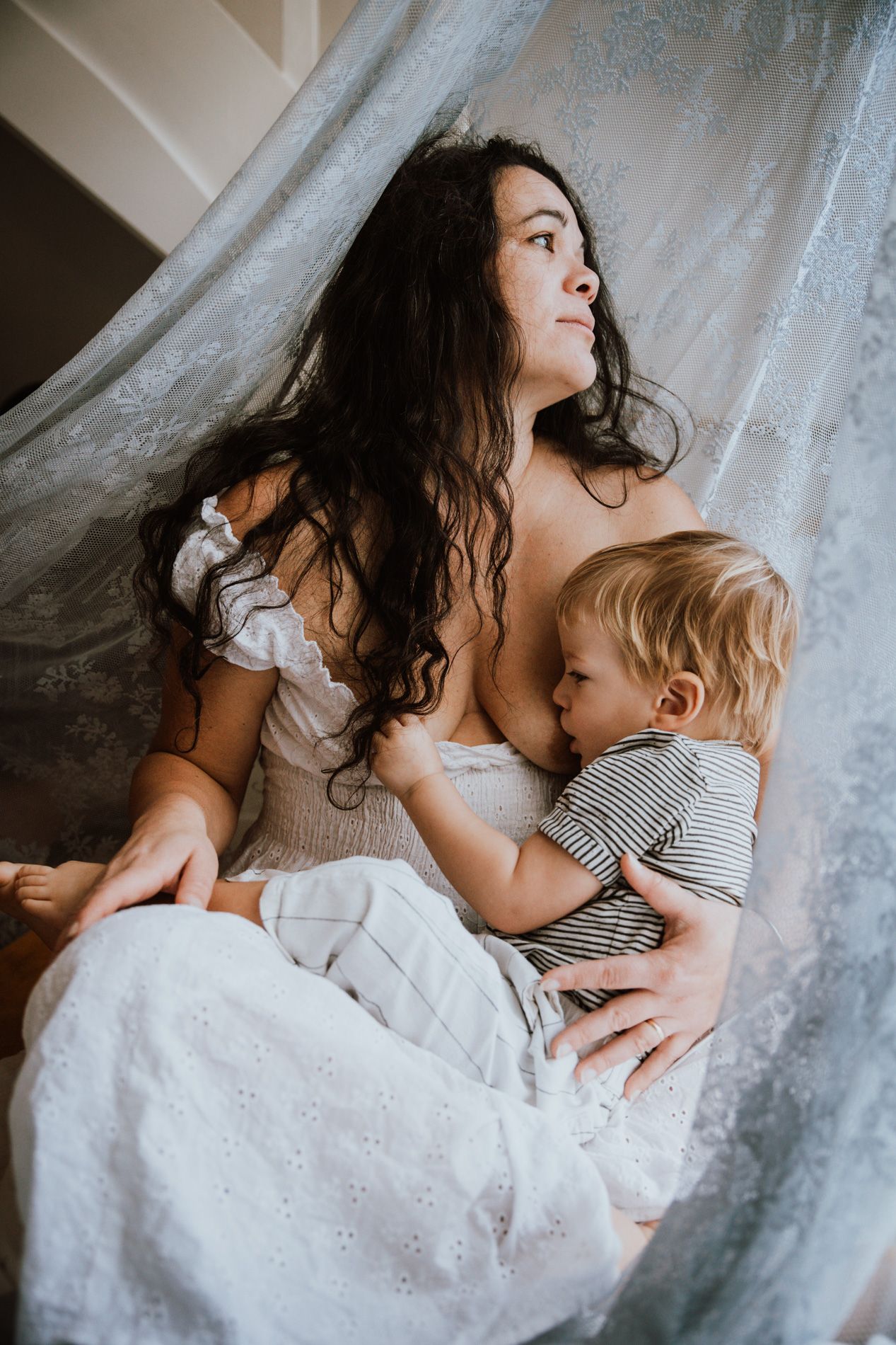 Tender moments captured in soft light as figures rest together on white bedding with delicate lace details.