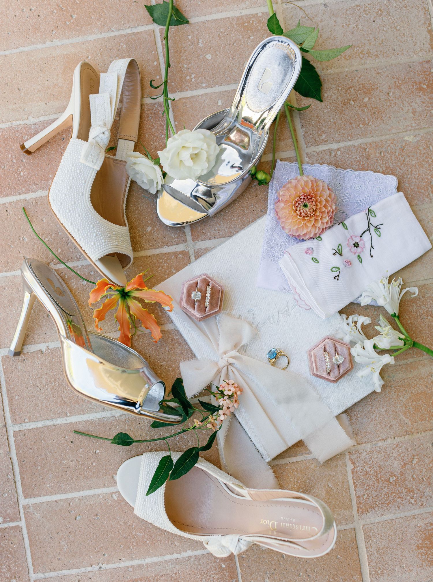 Wedding accessories including white heels, handkerchiefs, flowers, and perfume arranged on a beige tile floor.