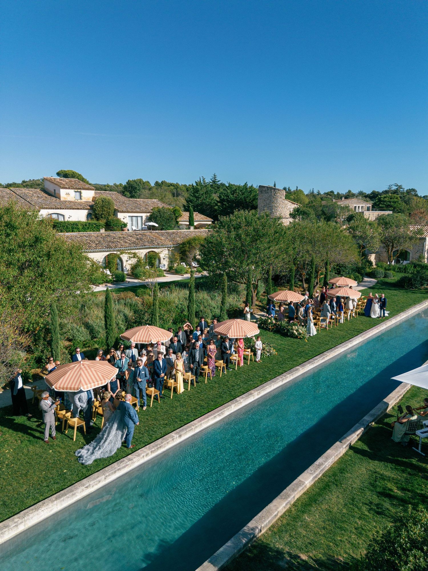 Aerial view of an outdoor wedding ceremony with guests seated in rows and a covered gazebo at the end of a long walkway.