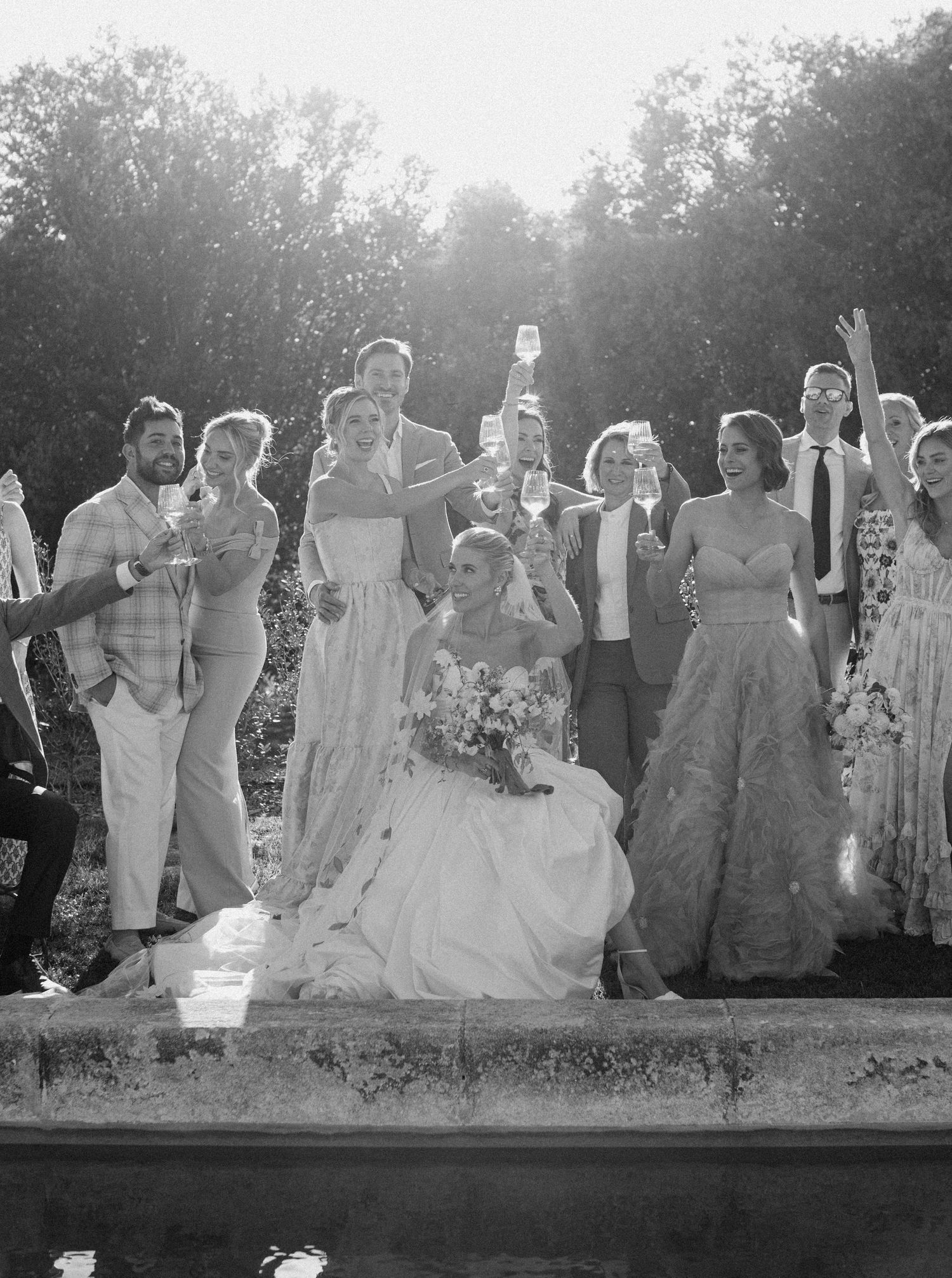 A black and white panoramic photo shows a large wedding party posing outdoors in formal attire.