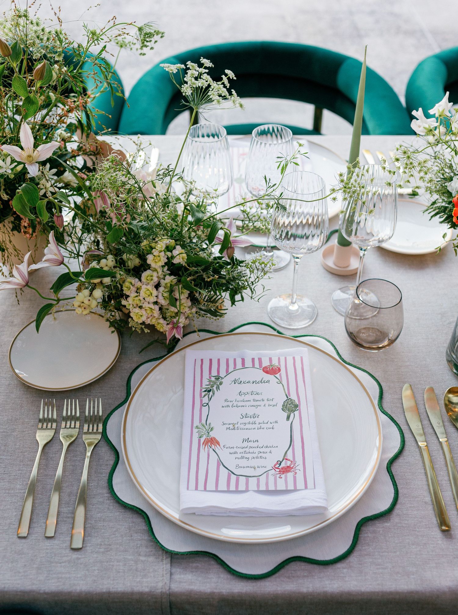 Elegant table setting with scalloped green-rimmed plates, floral menu cards, and delicate greenery centerpieces.