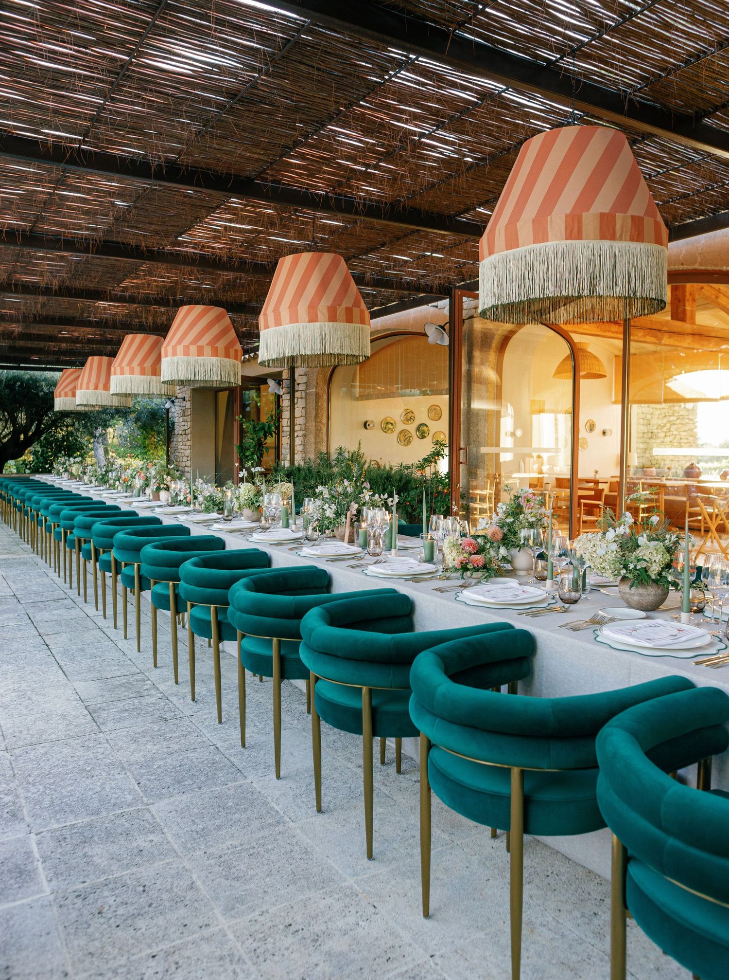 Elegant restaurant interior with curved emerald green velvet banquette seating and brass accents under a rustic wooden ceiling.