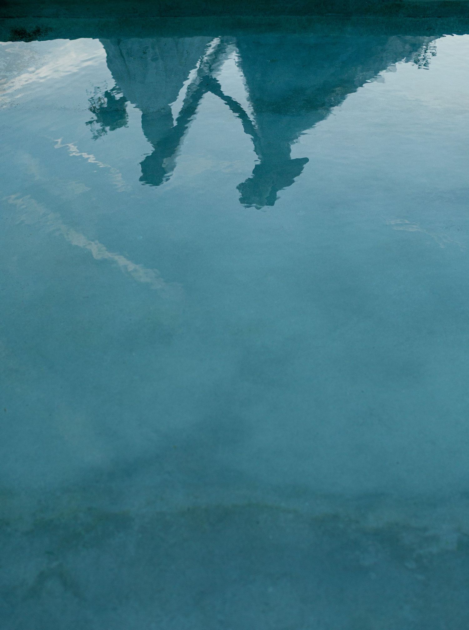 Abstract reflections create a tranquil blue-green pattern on rippling water surface in natural light.