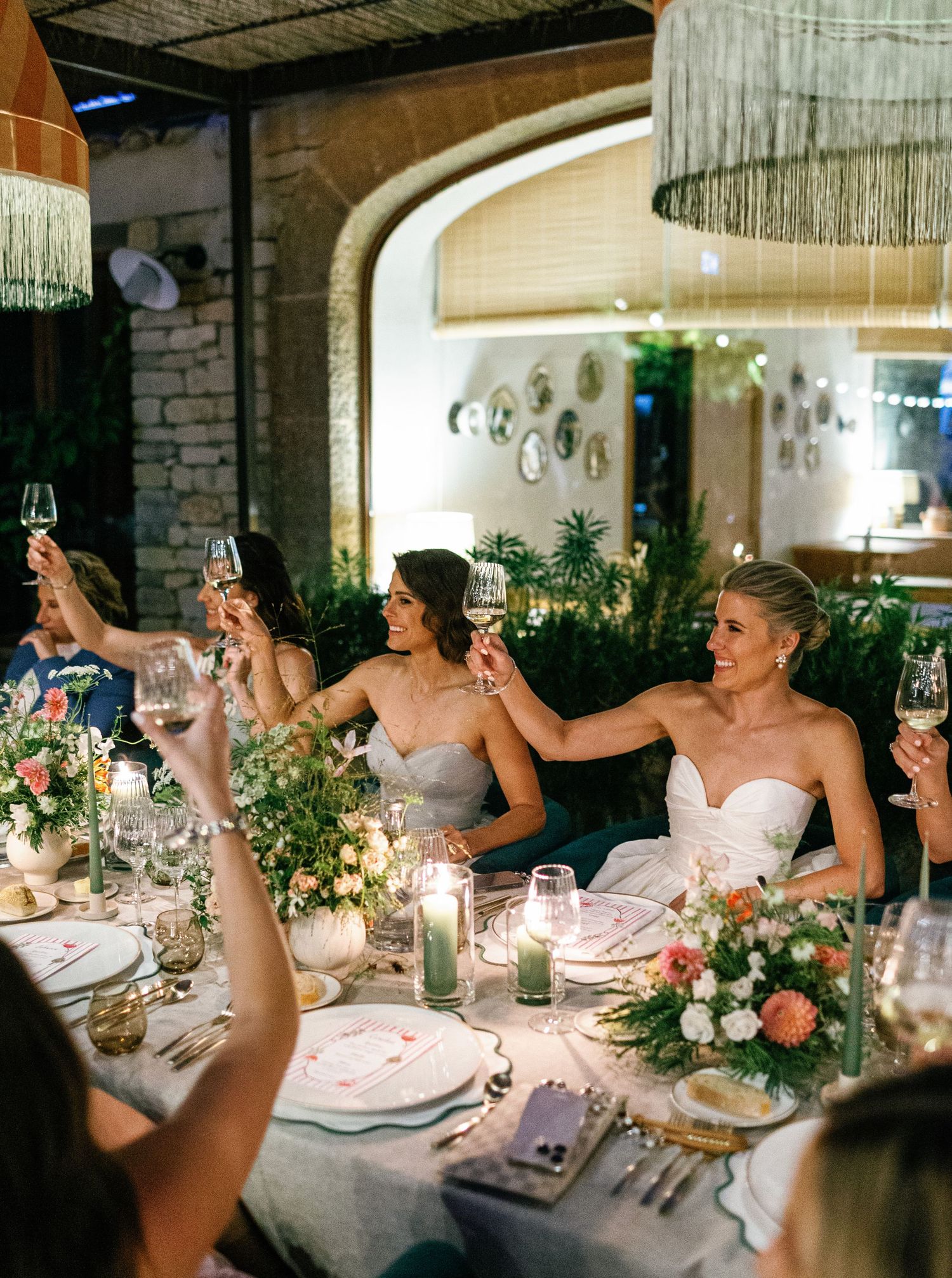 Wedding guests raise glasses in celebration at an elegant reception dinner table decorated with floral centerpieces.
