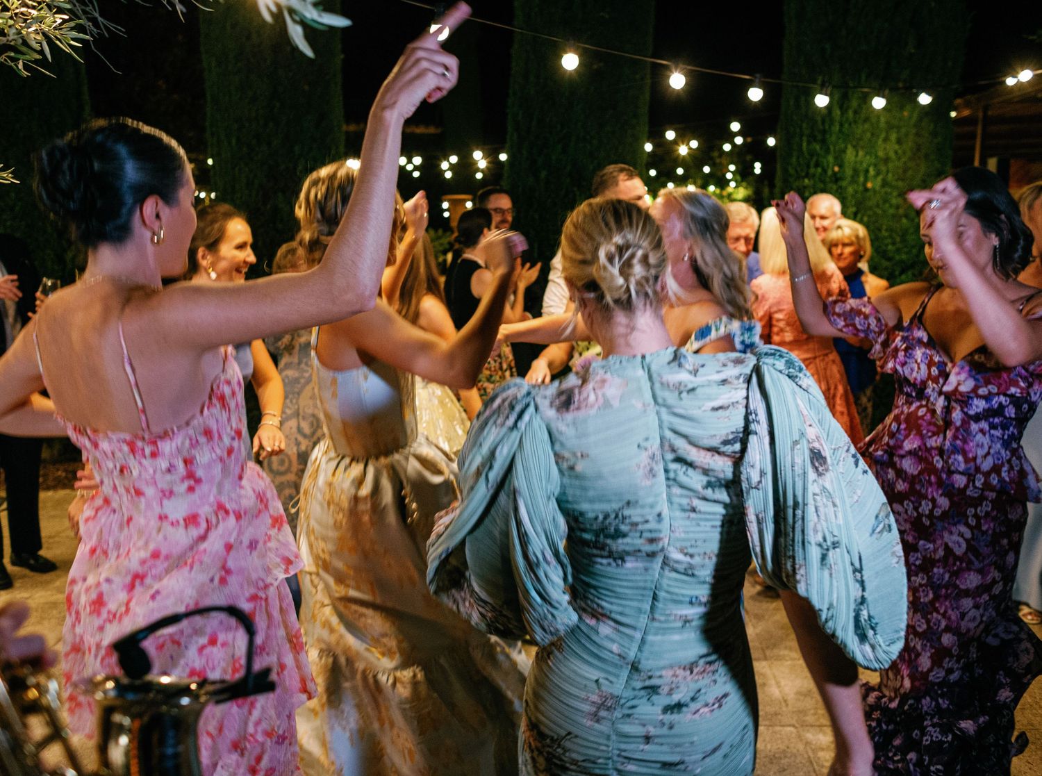People dancing and celebrating at an outdoor evening party with string lights illuminating the festive atmosphere.