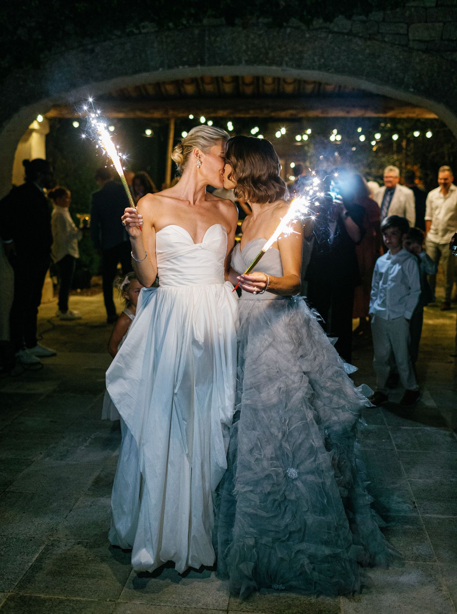 Wedding guests dance and celebrate at an outdoor evening reception with string lights overhead.