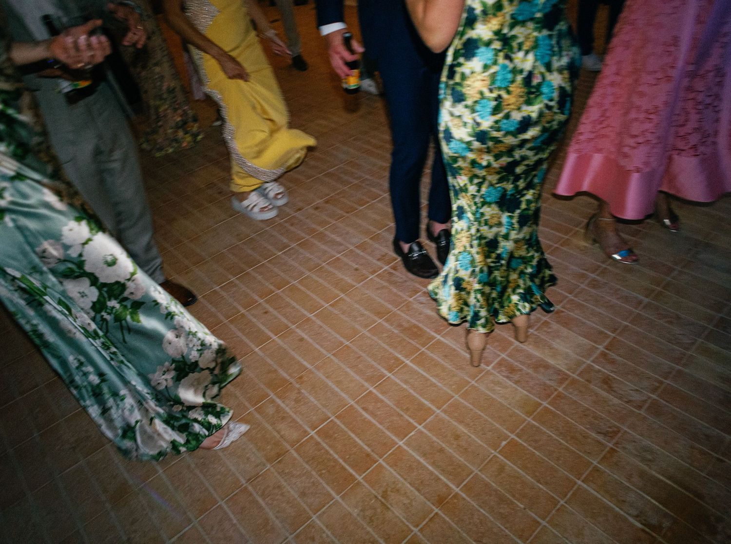 A group of dancers wearing floral dresses move across a wooden dance floor during a lively celebration.