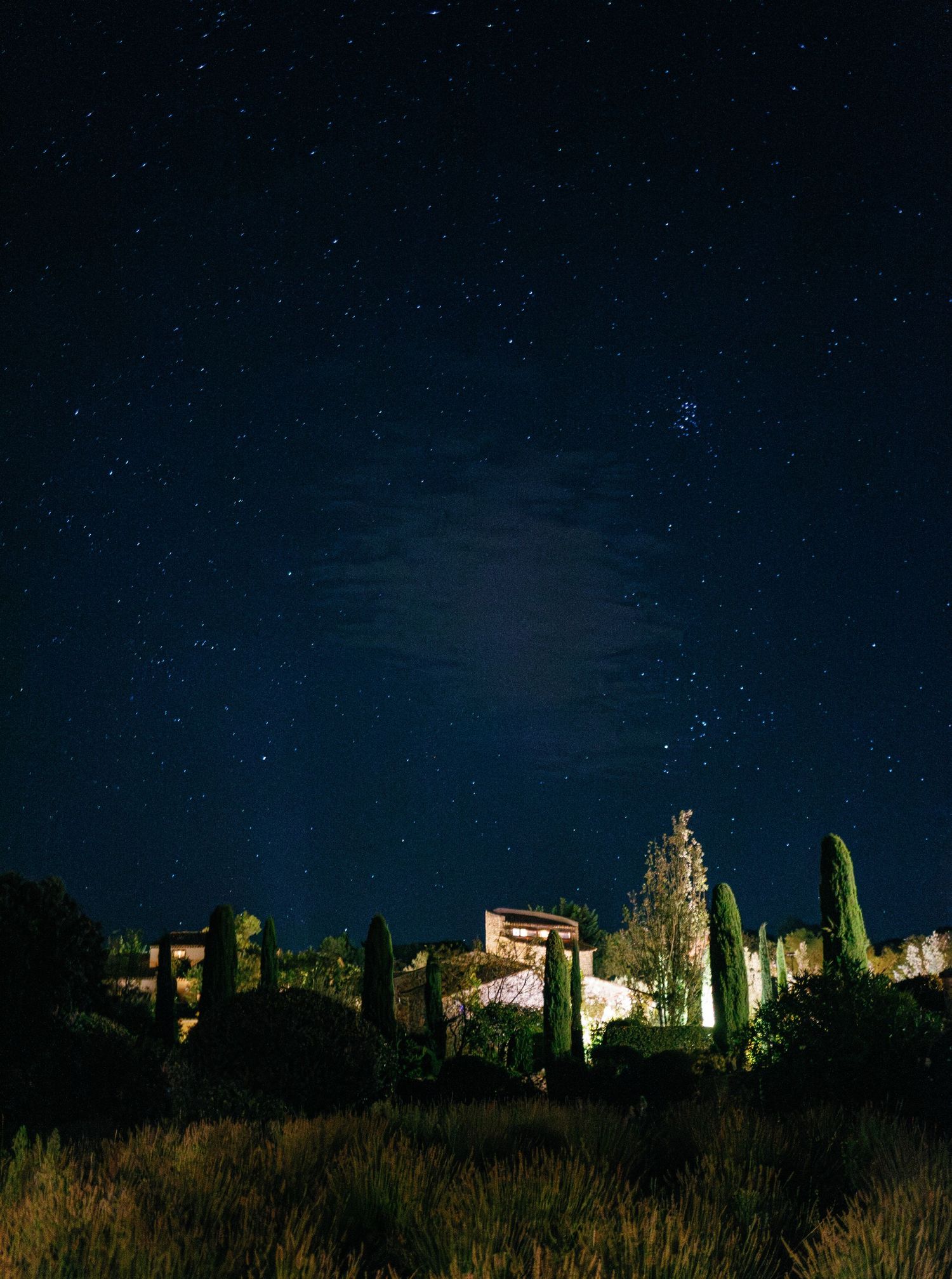 A panoramic view of Tuscan villas and cypress trees silhouetted against a starry night sky in Italy.