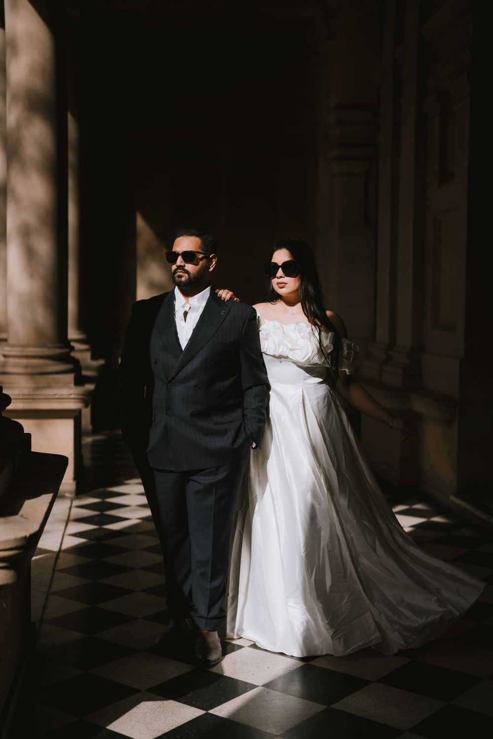 A dramatic wedding photo series in a dark hallway with columns showing contrast between black suit and flowing white dress.