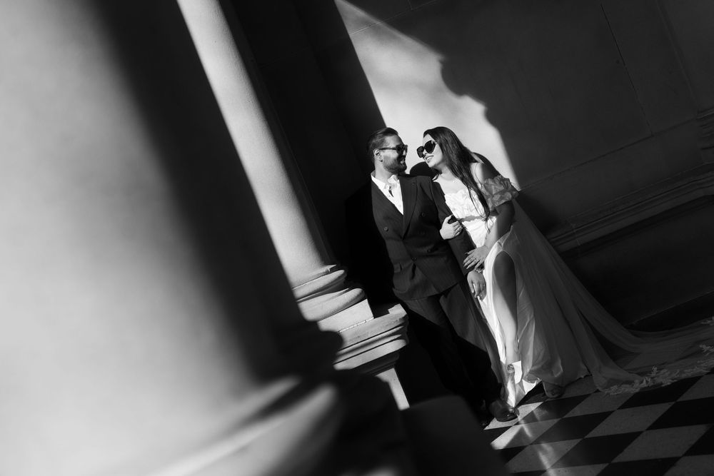 A dramatic black and white wedding photograph showing a couple on a checkered floor with dramatic shadows and lighting.