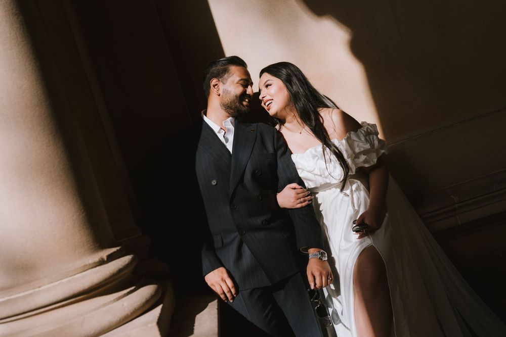 A couple in wedding attire share an intimate moment against a neutral backdrop in dramatic lighting.