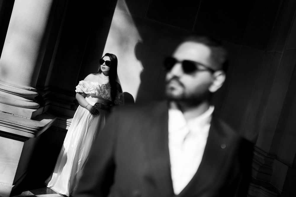 Artistic black and white wedding portrait with dramatic shadows and architectural elements.