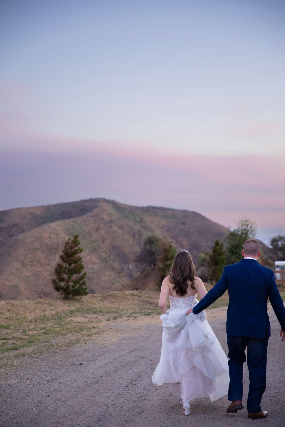 A bride and groom walking as the groom helps the bride with her wedding dress.