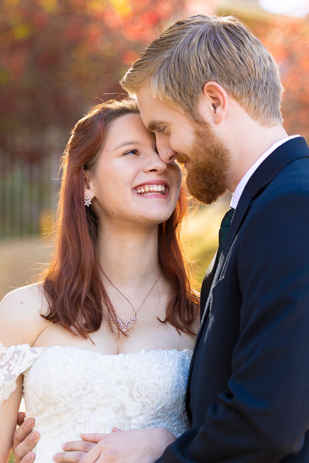 A bride and groom embracing one another while touching foreheads and looking at one another, smiling.