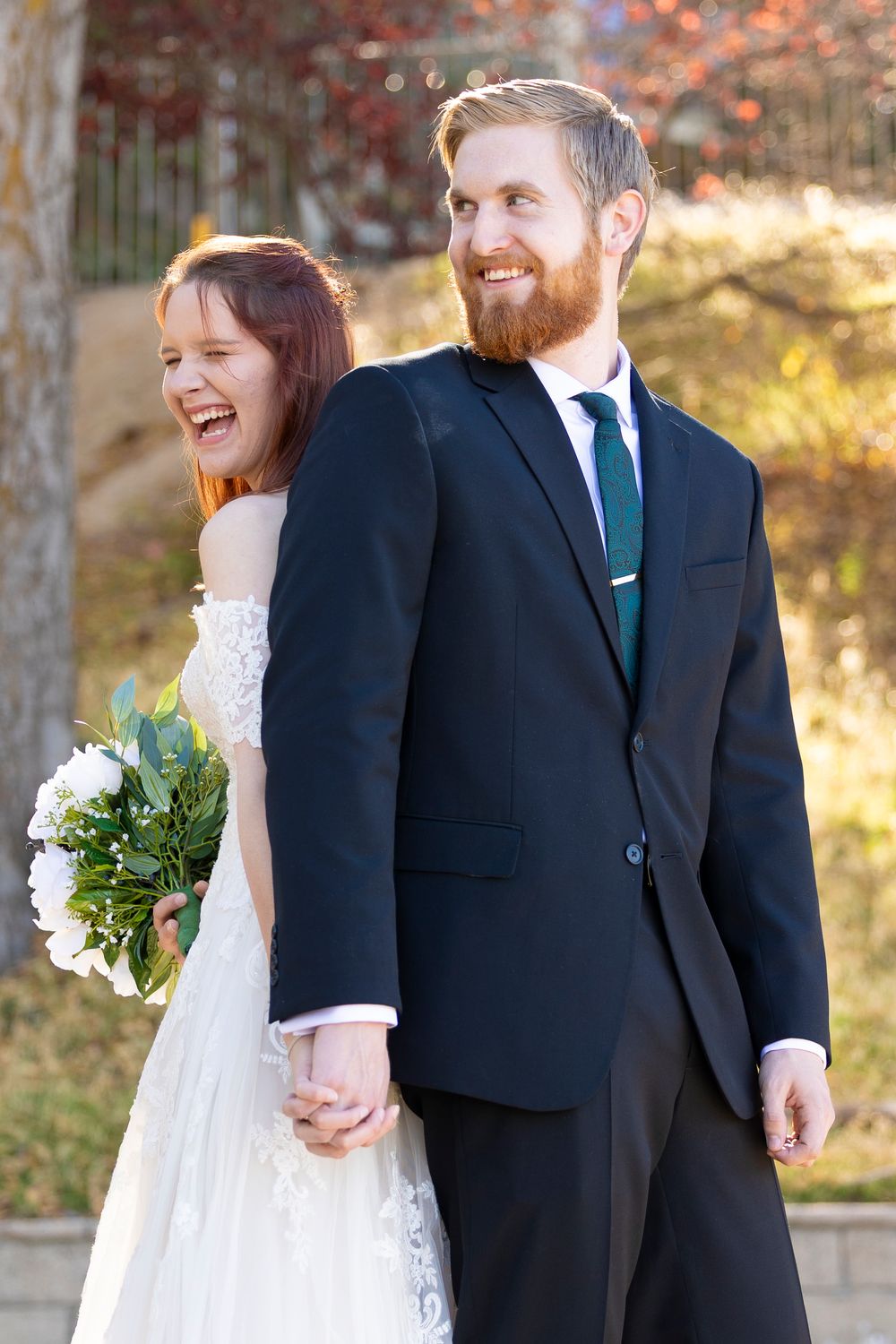 A bride and groom standing back to back while holding hands and smiling.