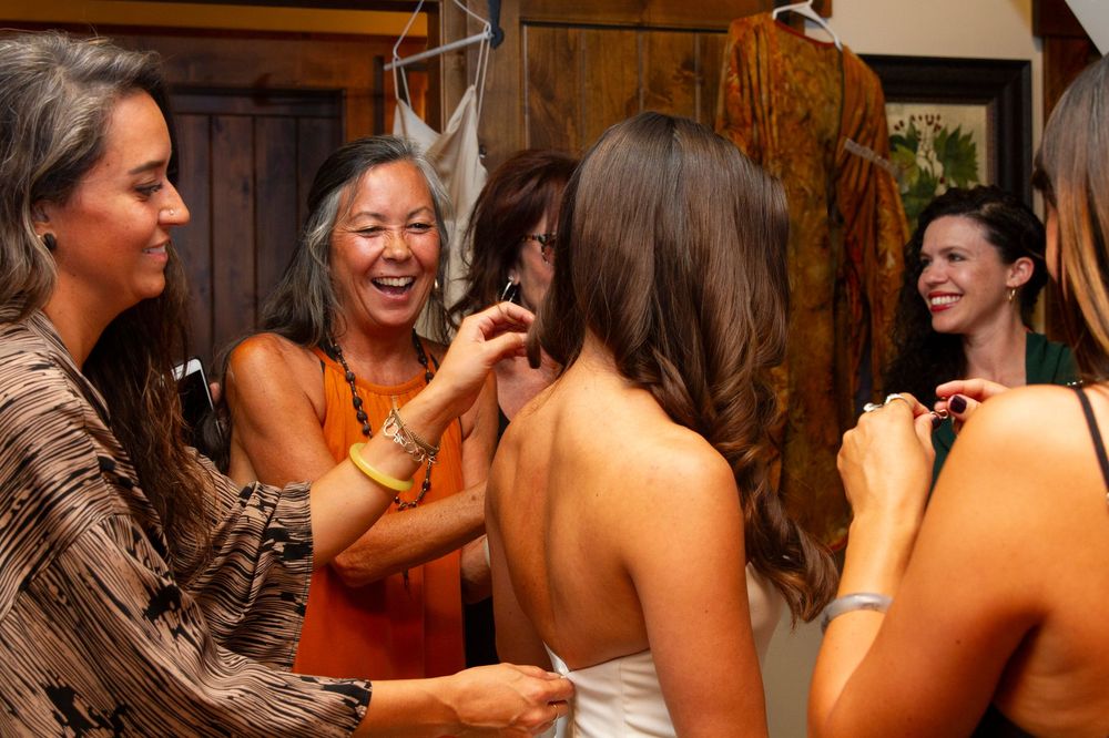 A bride getting ready surrounded by her wedding party as they help her with finishing touches.