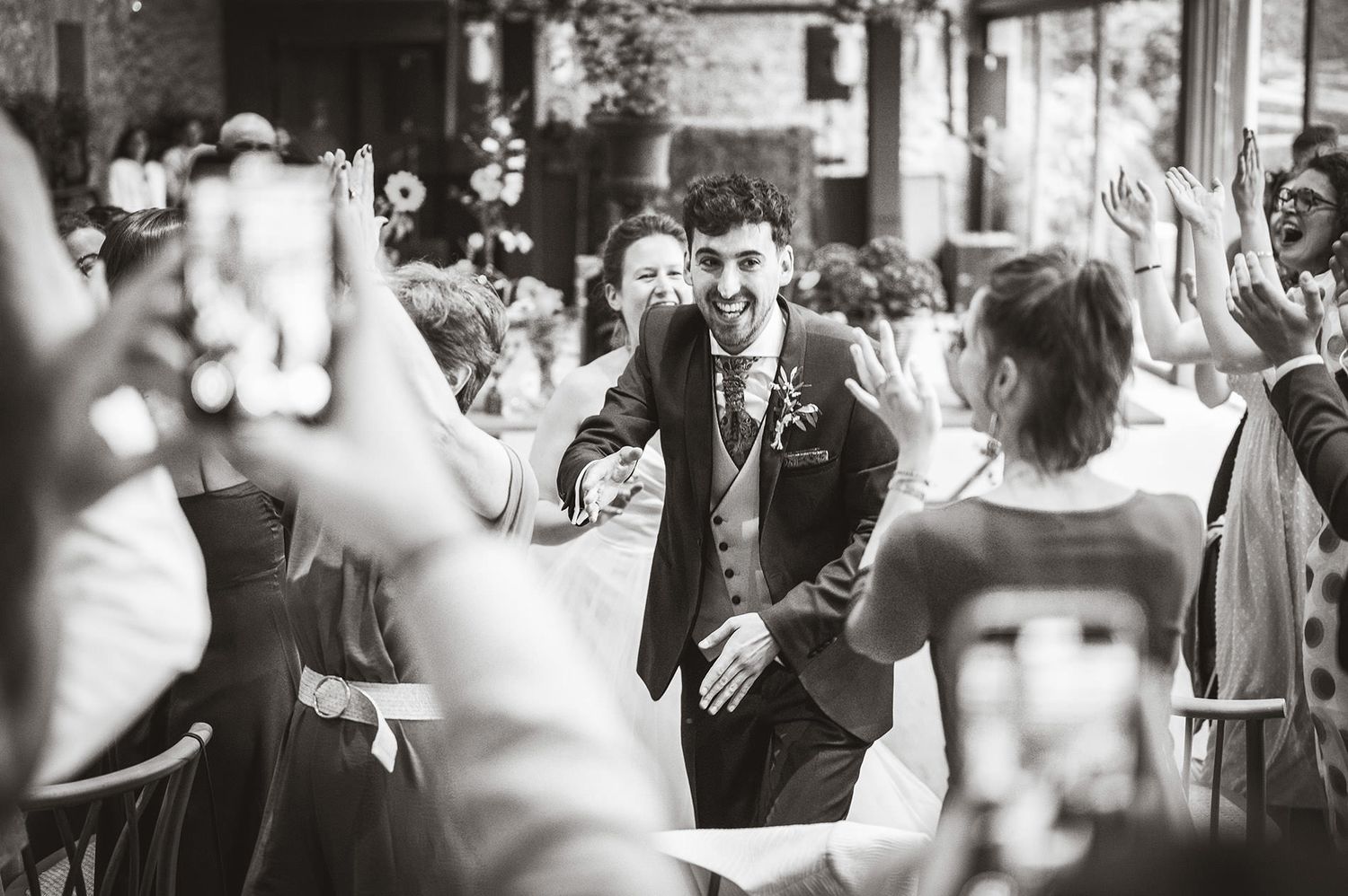 Novio avanzando entre mesas mientras los invitados aplauden y celebran su entrada al banquete durante una boda en Asturias.