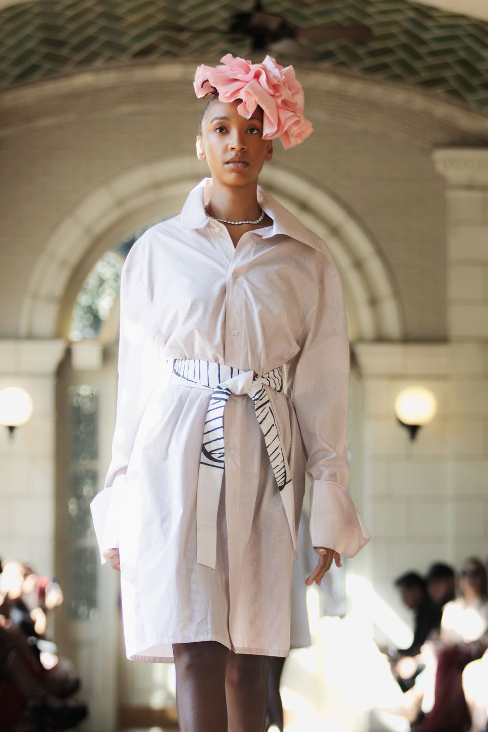 A model walks the runway in a white oversized shirt dress with bow details at a fashion show.