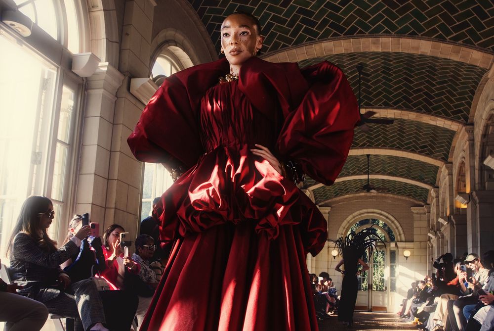 A group of performers in flowing red costumes dance and move dramatically in an ornate architectural space.