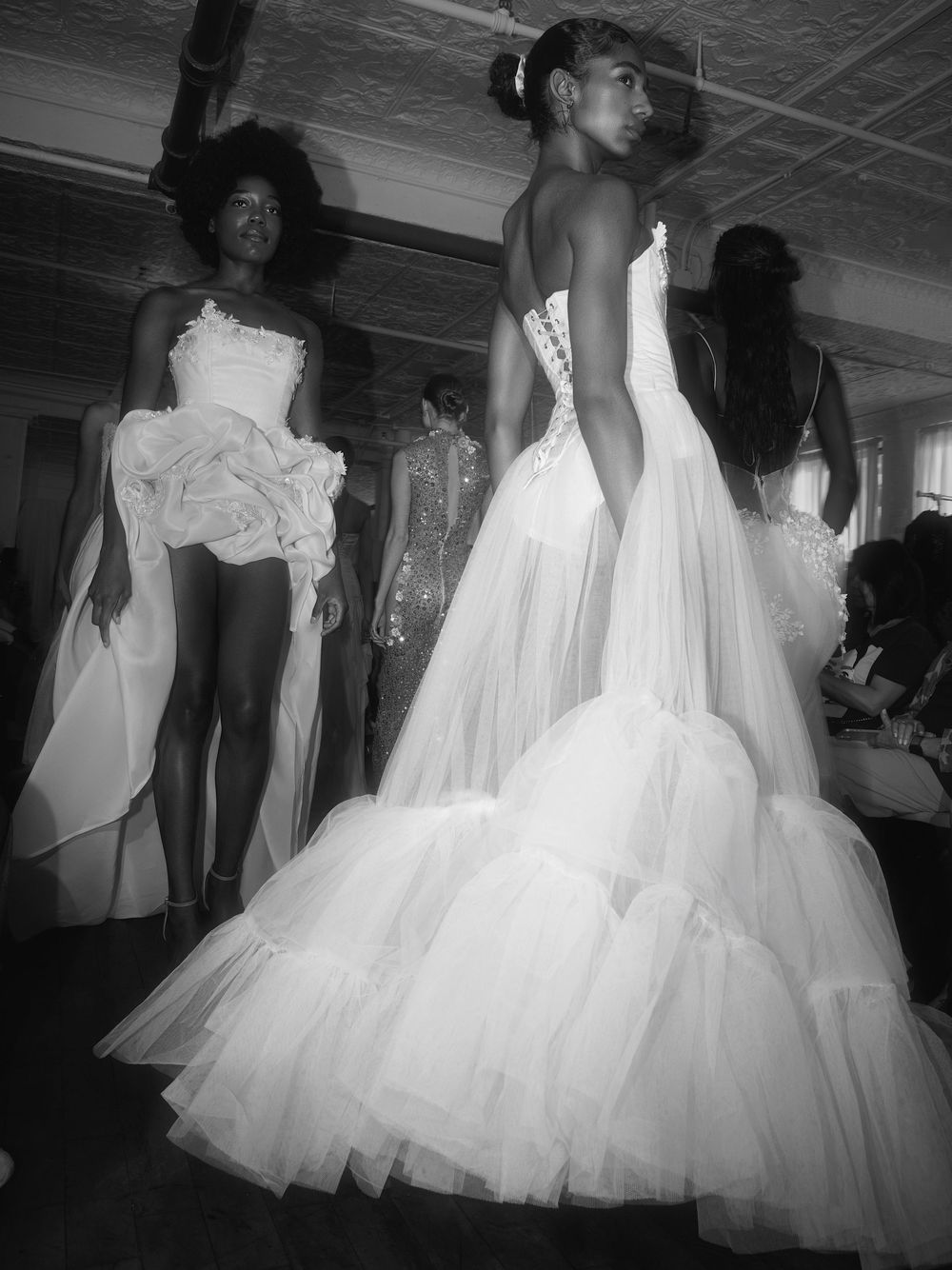 A collection of flowing white wedding dresses displayed in a dark room creating an ethereal fashion showcase effect.