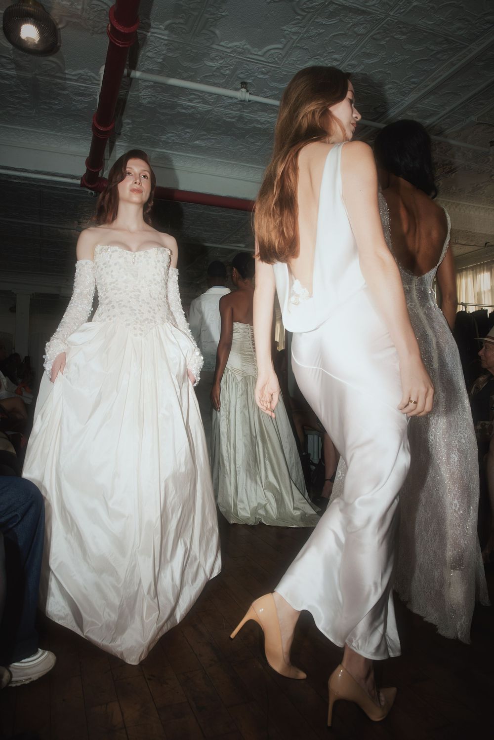 Multiple figures in white flowing dresses move through a dimly lit space creating an ethereal dance-like sequence.