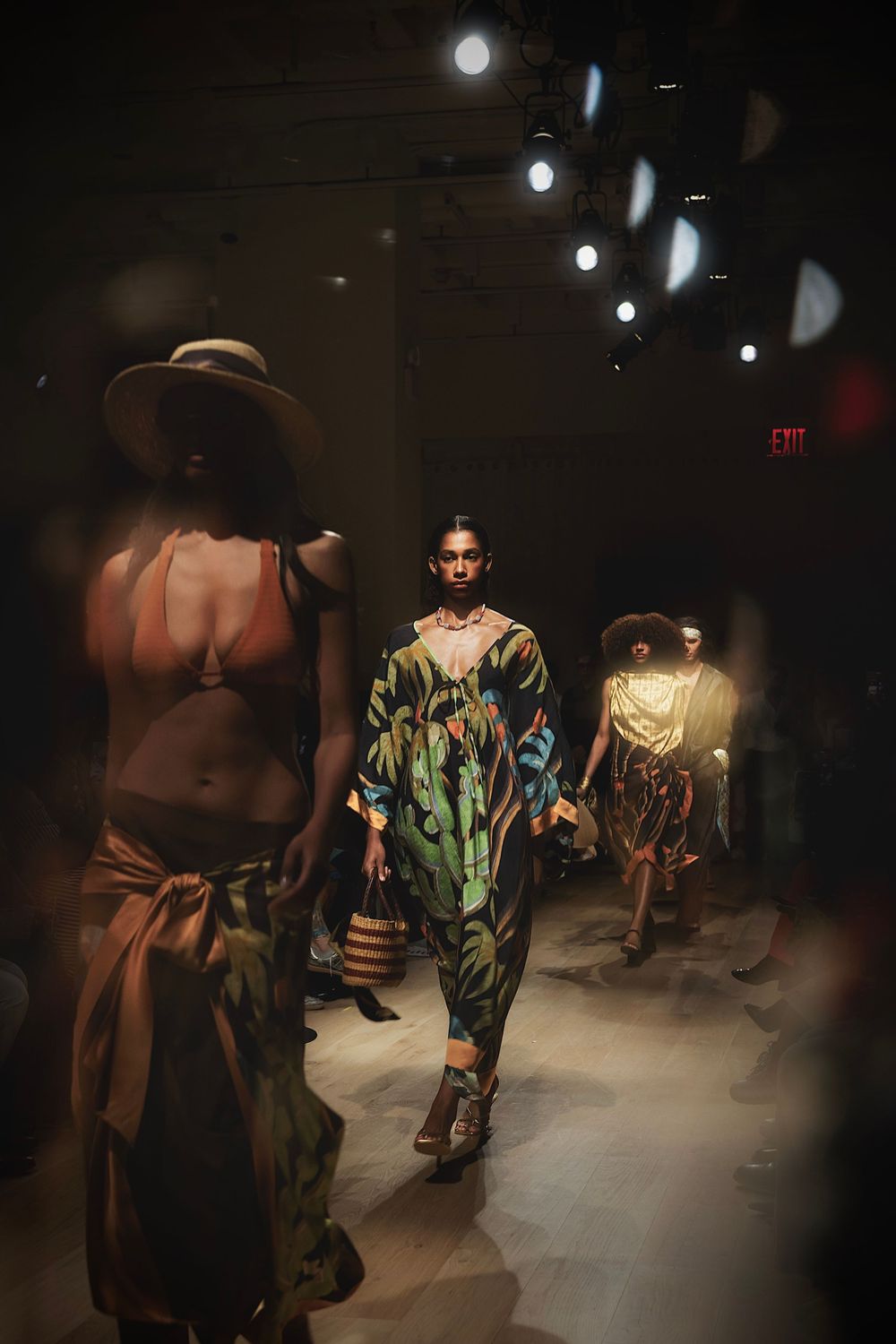 Models walk the runway showcasing avant-garde fashion designs in a dimly lit industrial space during a fashion show.
