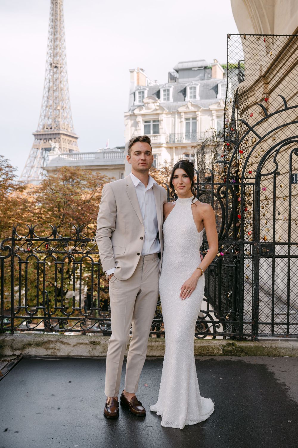 Elegant couple posing near ornate iron gates with the Eiffel Tower in the background.