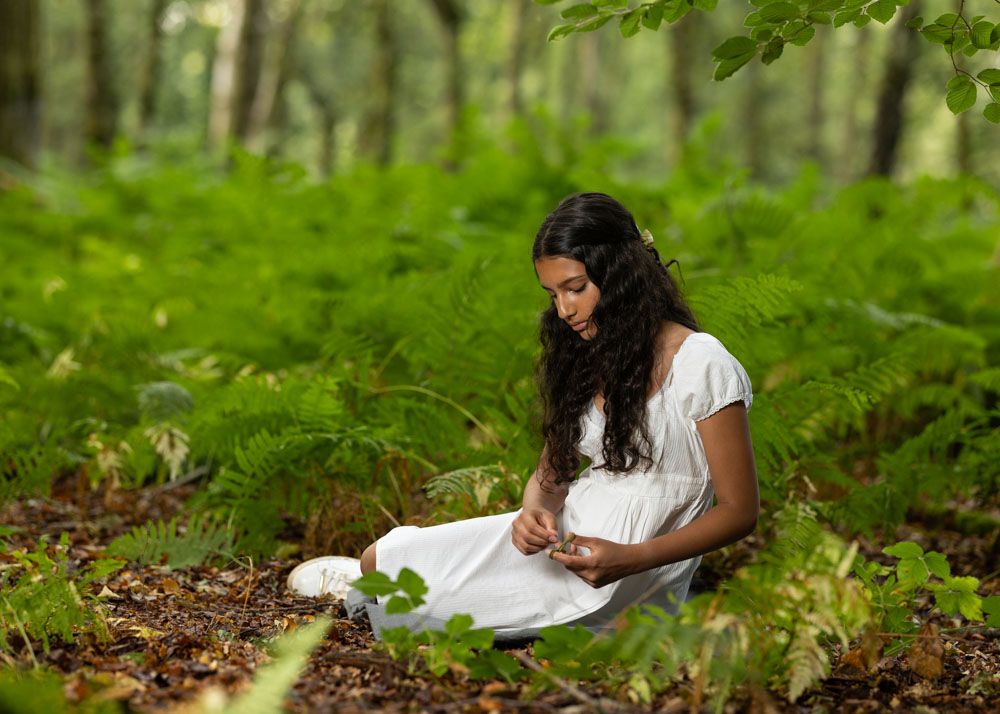 Stylish portrait of young girl in white dress in Kent woods sitting