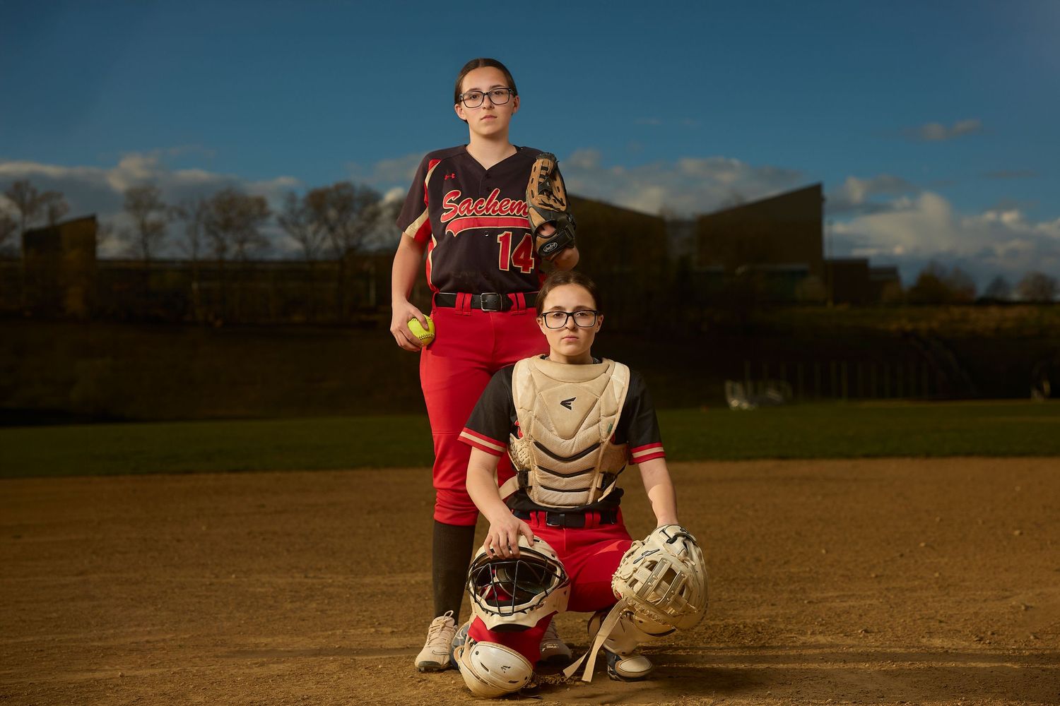 Youth baseball player in black and red uniform poses with arms crossed for dramatic sports portrait.