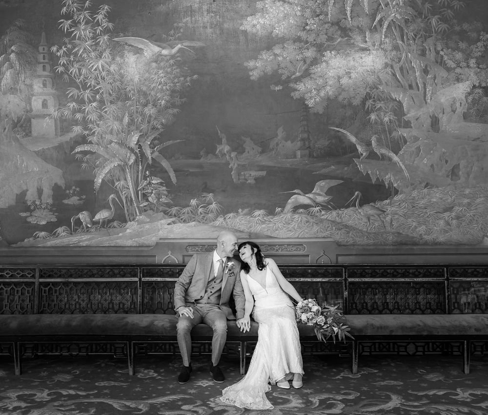 Bride and groom in Brighton Pavilion backed by huge tapestry