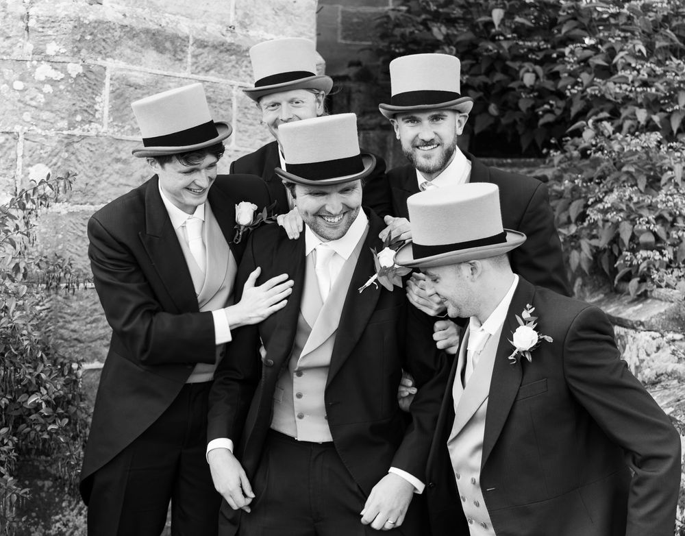 Groomsmen laughing and patting groom on the back at Wadhurst castle, East Sussex