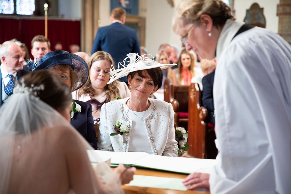 Mother of bride gracefully watches as bride signs register in old church
