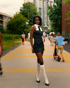 A stylish outfit featuring a pinstriped dress with white collar, knee-high socks and heels on a yellow-striped walkway.