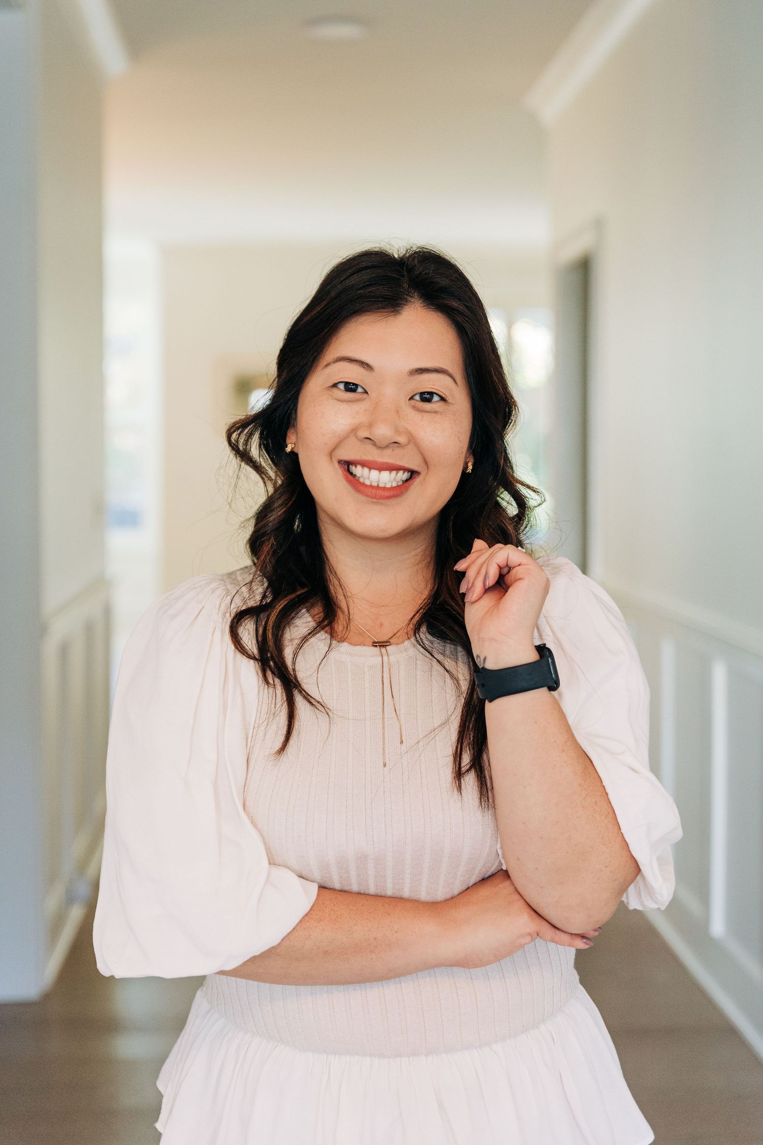 A realtor in white poses in a bright hallway with white walls and natural lighting for Charlotte headshots