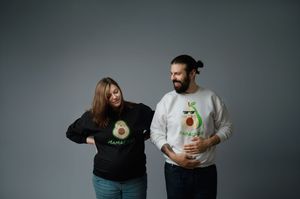 Two people wearing matching avocado graphic shirts pose together against a gray background.