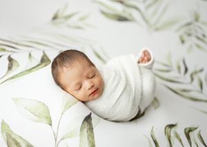 A peaceful sleeping newborn swaddled in white lying on a botanical print background.