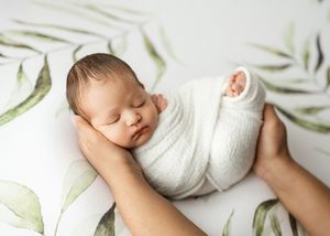A peacefully sleeping newborn wrapped in white swaddle on a soft floral backdrop.
