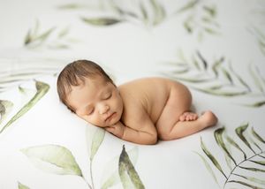 Peaceful sleeping newborn curled up on soft white fabric with delicate green botanical print pattern.